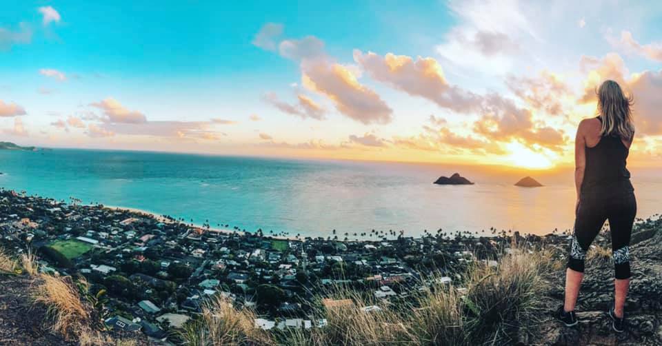 Woman looking out at Lanikai Beach as she is on the edge of Lanikai Pillbox trail at sunrise. Travel tips for beginners