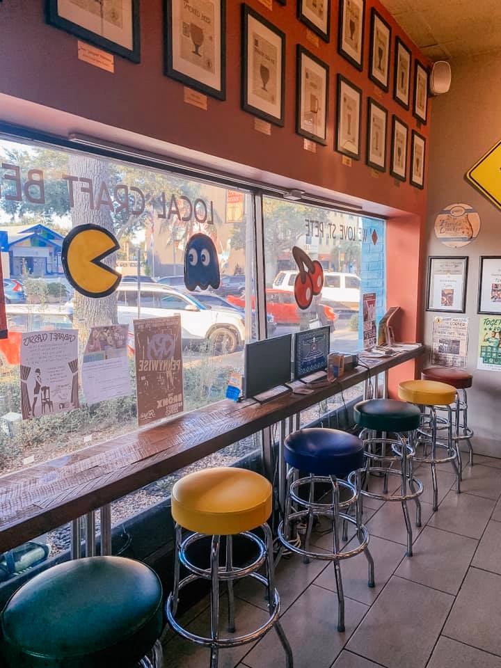 several different colored stools set up at a table lining a window with a view of outside through a Pacman decorated window