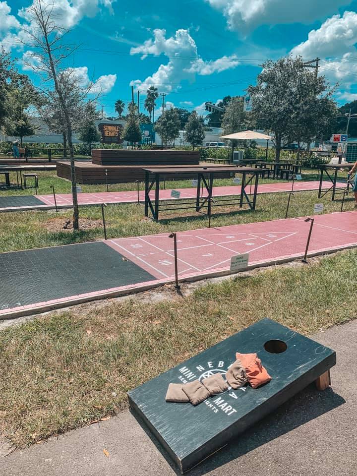 A sunny day with an outdoor setup of corn hole and shuffleboard