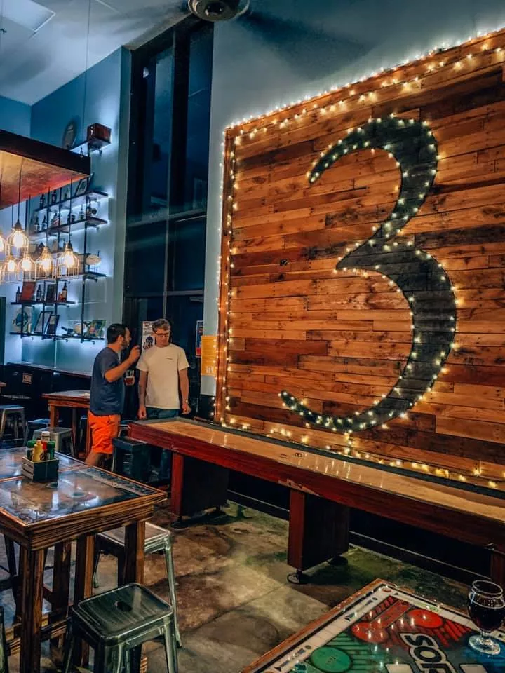 Wall covered with the number 3 outlined in lights.  Game of shuffleboard being played in front.