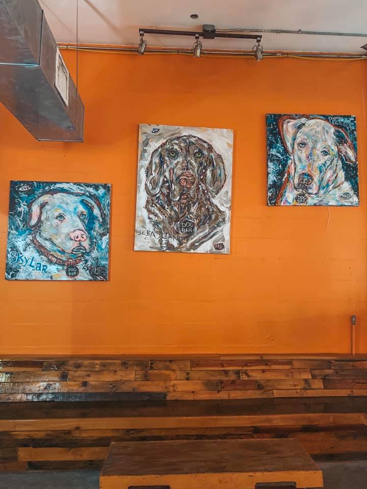 An orange wall with three somewhat abstract paintings of three different breeds of dogs.