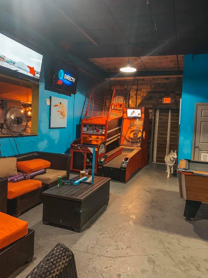 A blue room with seating as well as pool, skeeball, and basketball.  As well as a husky wandering around.