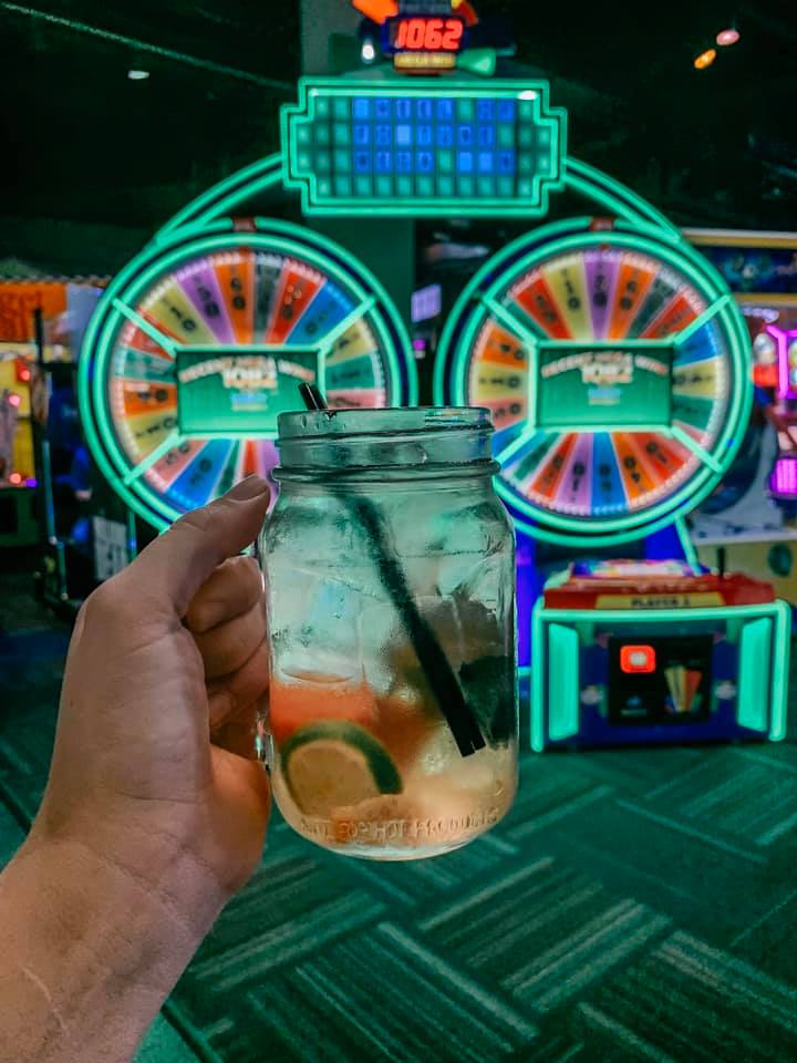 A hand holding up a watermelon and mint sangria in front of a wheel of fortune game at Gametime, a fun bar in Tampa