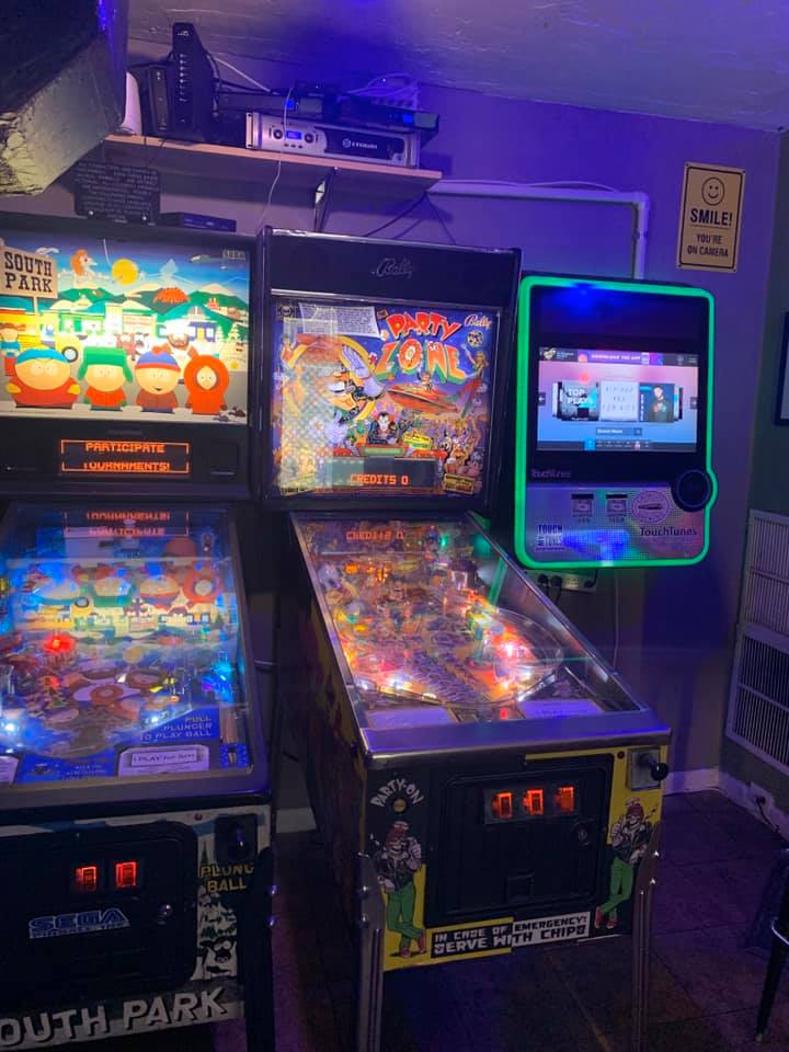 2 pinball machines next to a touchtunes jukebox