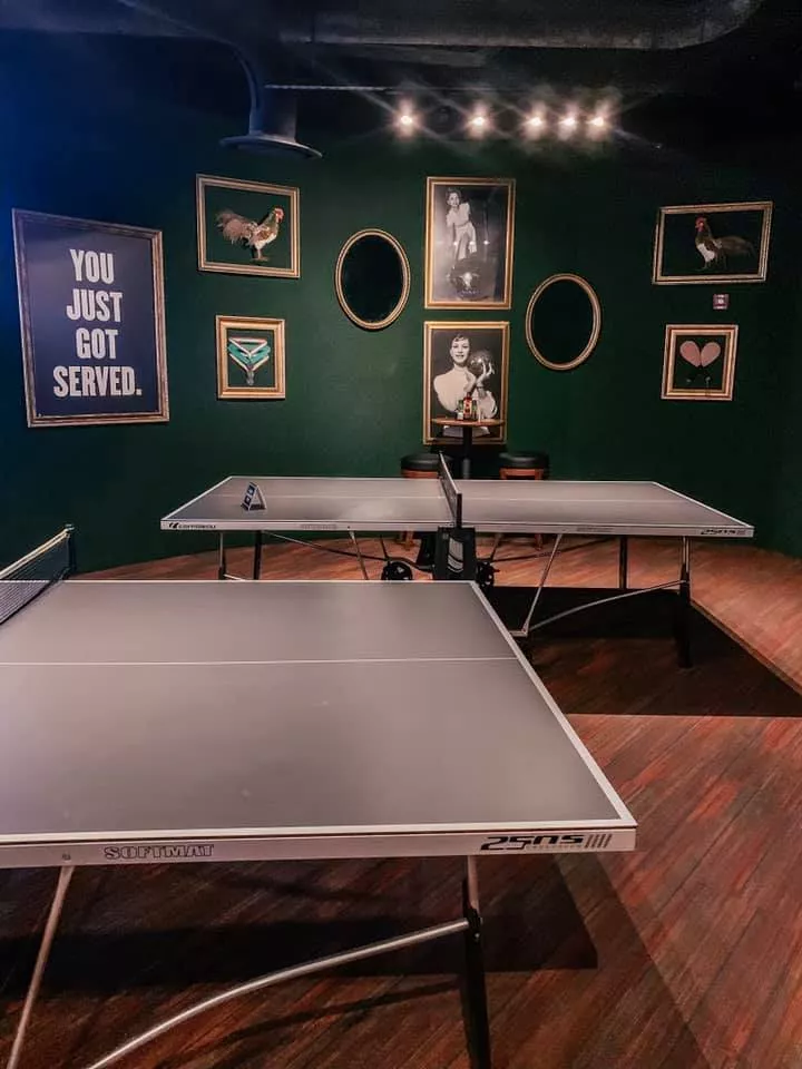 two ping pong tables set up in a green room with portrait covered walls