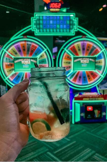holding up a cocktail in front of Wheel of Fortune game at Gametime in Ybor Tampa