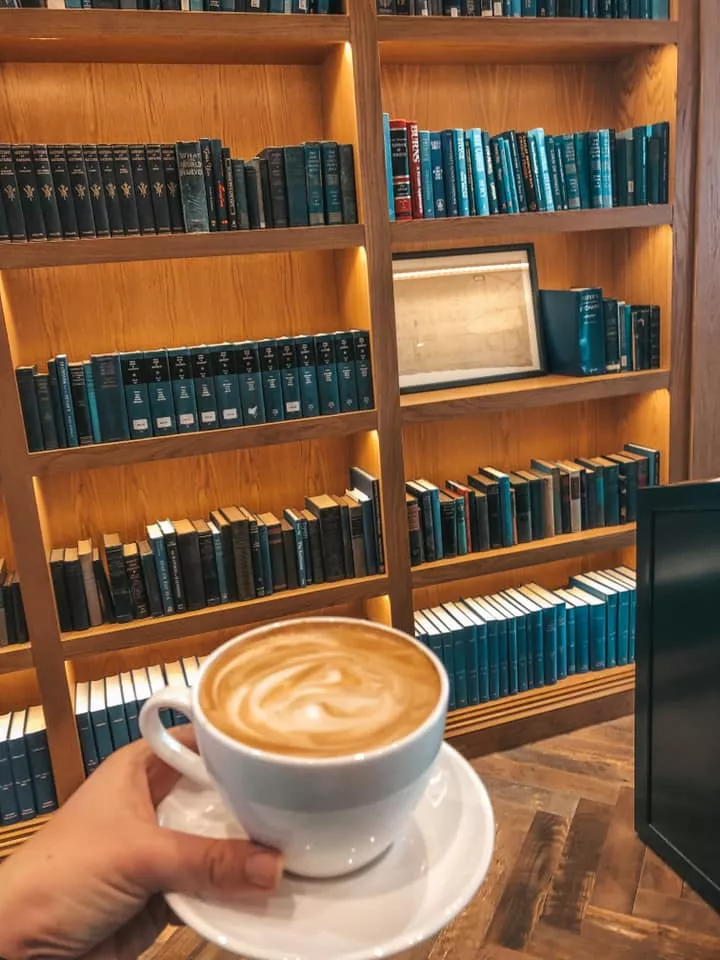 holding latte in front of book shelf full of blue books at coffee shops in St. Petersburg, Florida