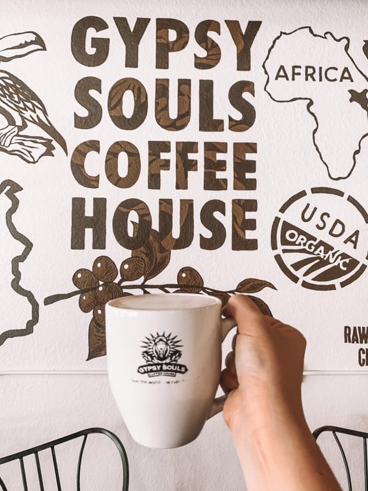 coffee mug that says "gypsy souls" being held up in front of wall mural that says "gypsy souls coffee house"