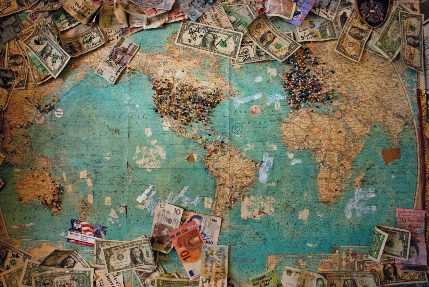world map with money and pins on it. Travel insurance costs, but it is important to have.