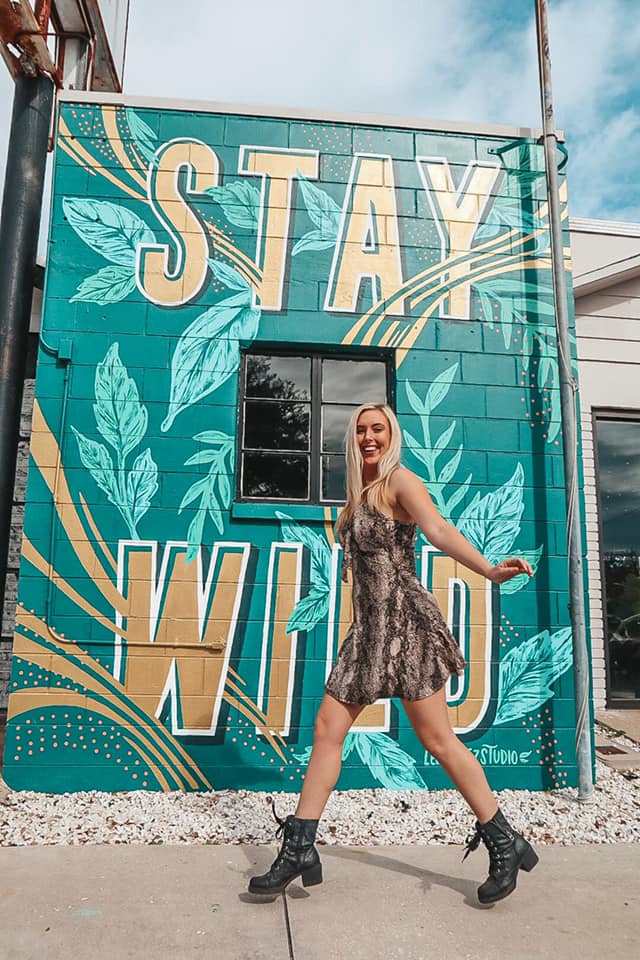 Jumping in a cheetah dress in front of a mural that says "Stay Wild"