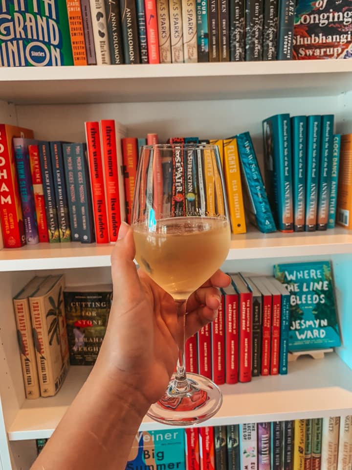 Glass of book + bottle's pinot grigio in front of some of their book selection