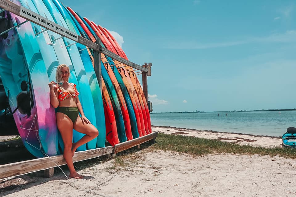 woman in a bathing suit leaning against colorful kayaks in Dunedin, Florida