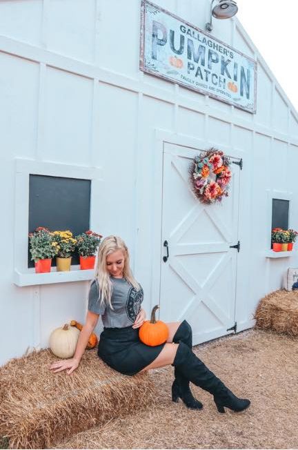 Woman posing on a haystack in front of a white barn at Gallaghers Pumpkin Patch in St. Pete