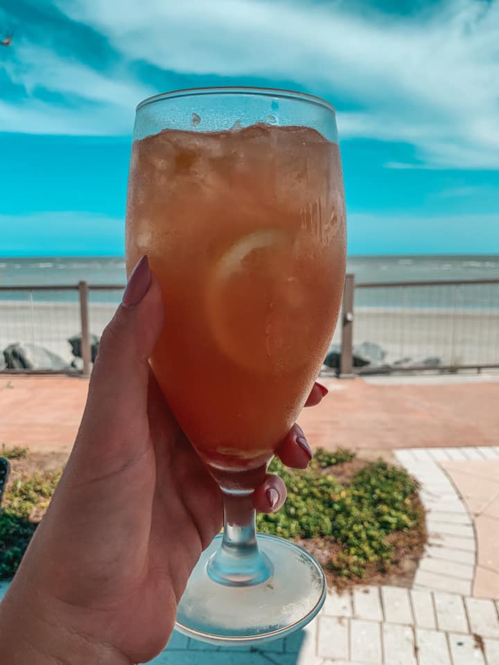 White peach sangria held up to the ocean in the background. Relaxing things to do in St. Simons Island, Georgia