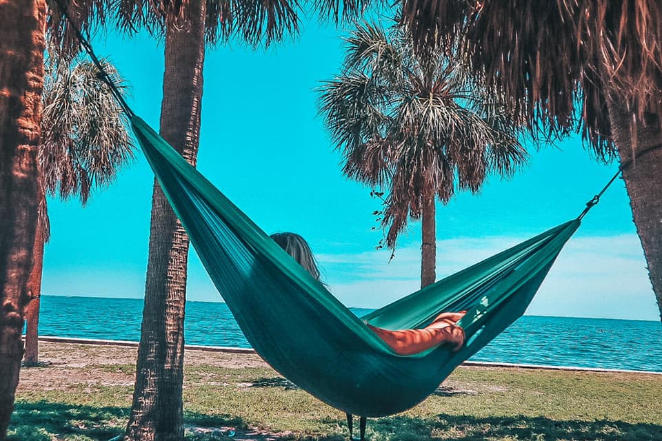 Woman relaxing on a green hammock held up by two palm trees