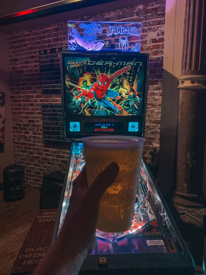Beer being held in front of pinball machine at Lowry Parcade