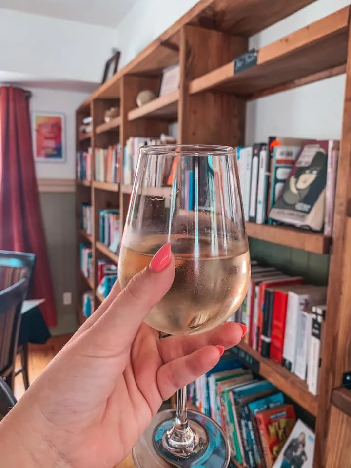 Glass of white wine held up in front of books at The Reserve