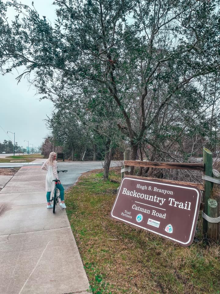 Sitting on bicycle in front of trail sign for the Hugh S Branyon Trail at Gulf State Park. One of my favorite things to do in Orange Beach