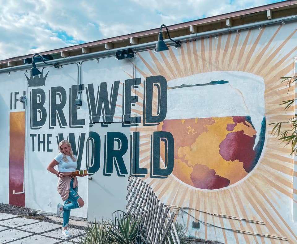 Holding beer flight in front of "If I brewed the world" mural