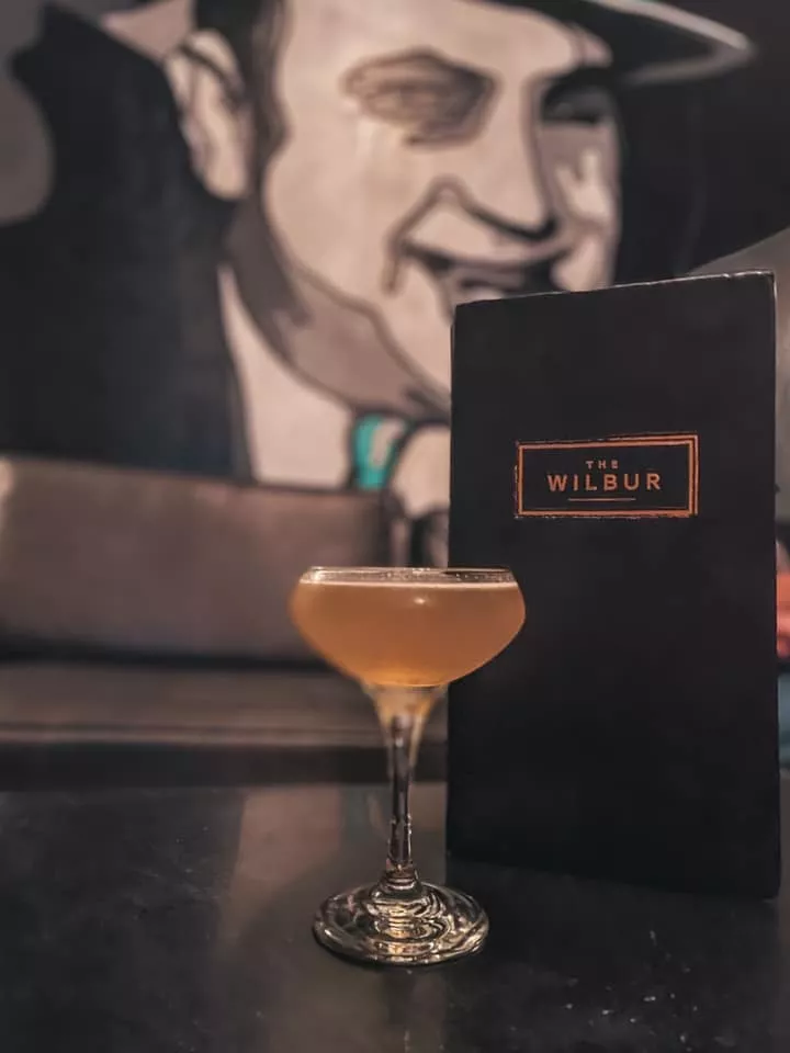 Cocktail from The Wilbur in front of menu and Al Capone art in the background