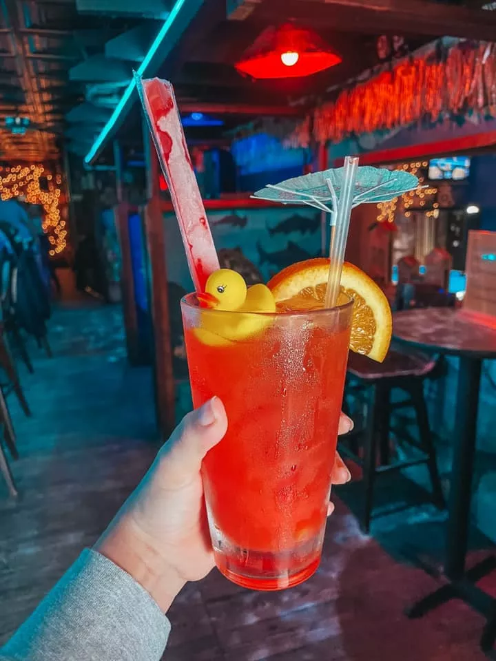 Fun orangish pinkish drink with an orange slice, ducky, and freeze pop sticking out of it