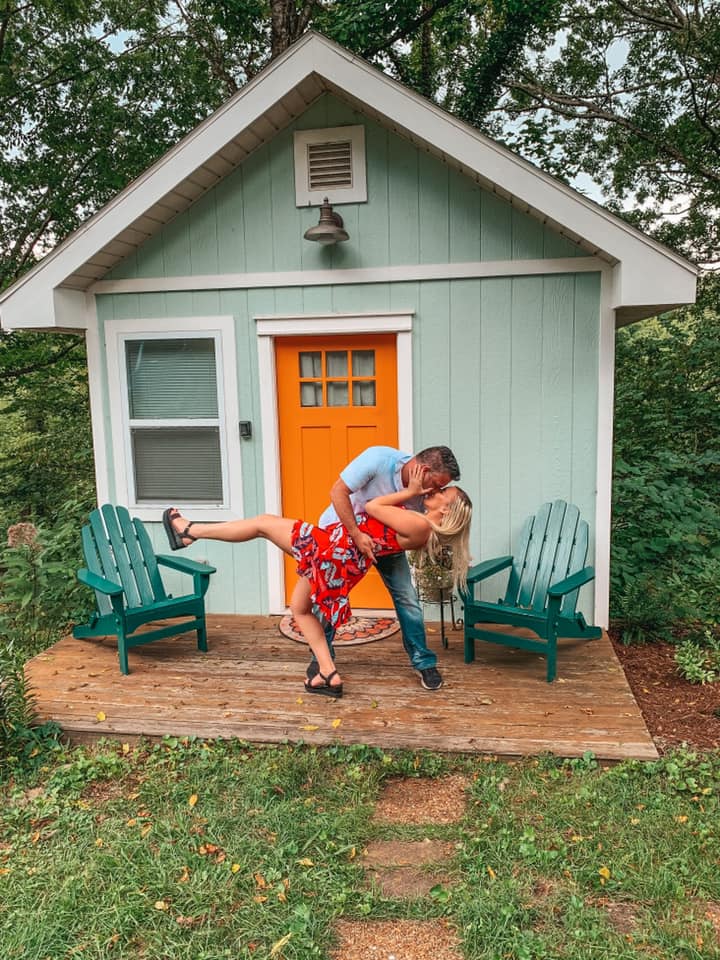 Man dipping and kissing a woman in front of a tiny home in Asheville