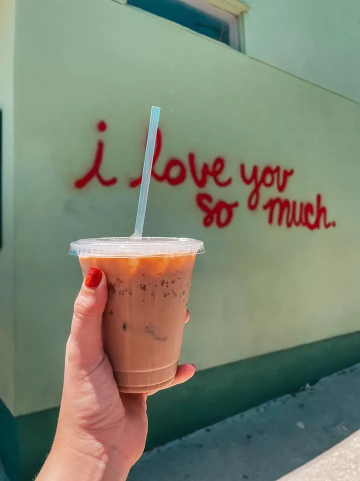 Holding up Jo's Coffee in front of I love you so much one of the things to Do in Austin