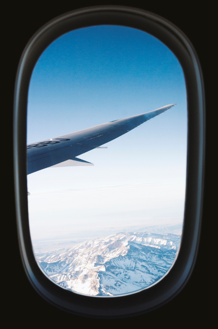 looking outside of the plane window at mountains during a flight where it's their first time traveling alone