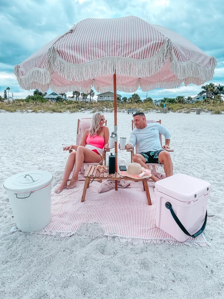sitting under pink and white striped umbrella for a beach day date