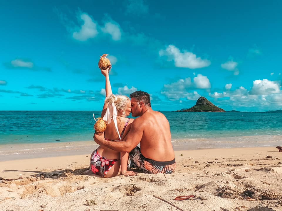 Couple kissing while holding coconuts on a beach in Oahu