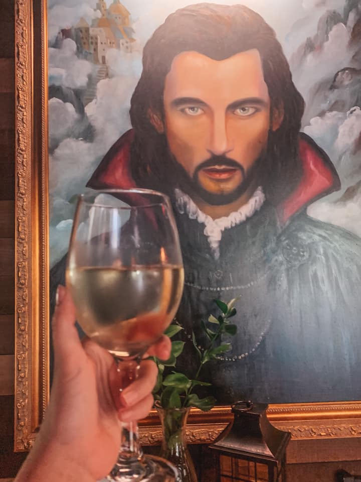 Wine glass with white wine held up in front of Dracula's picture