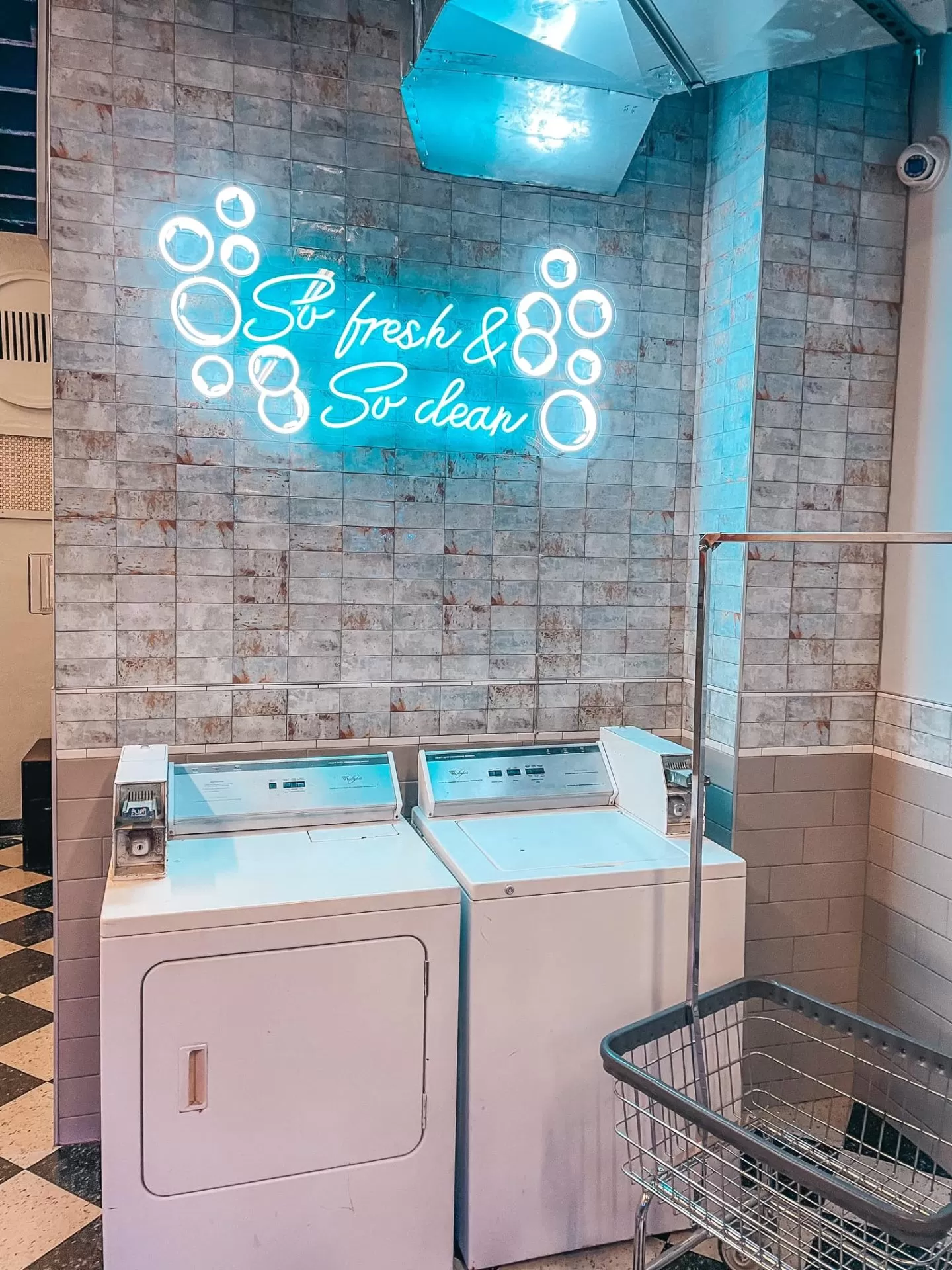 Neon sign that says "so fresh, so clean" above washer and dryer at Dirty Laundry Speakeasy