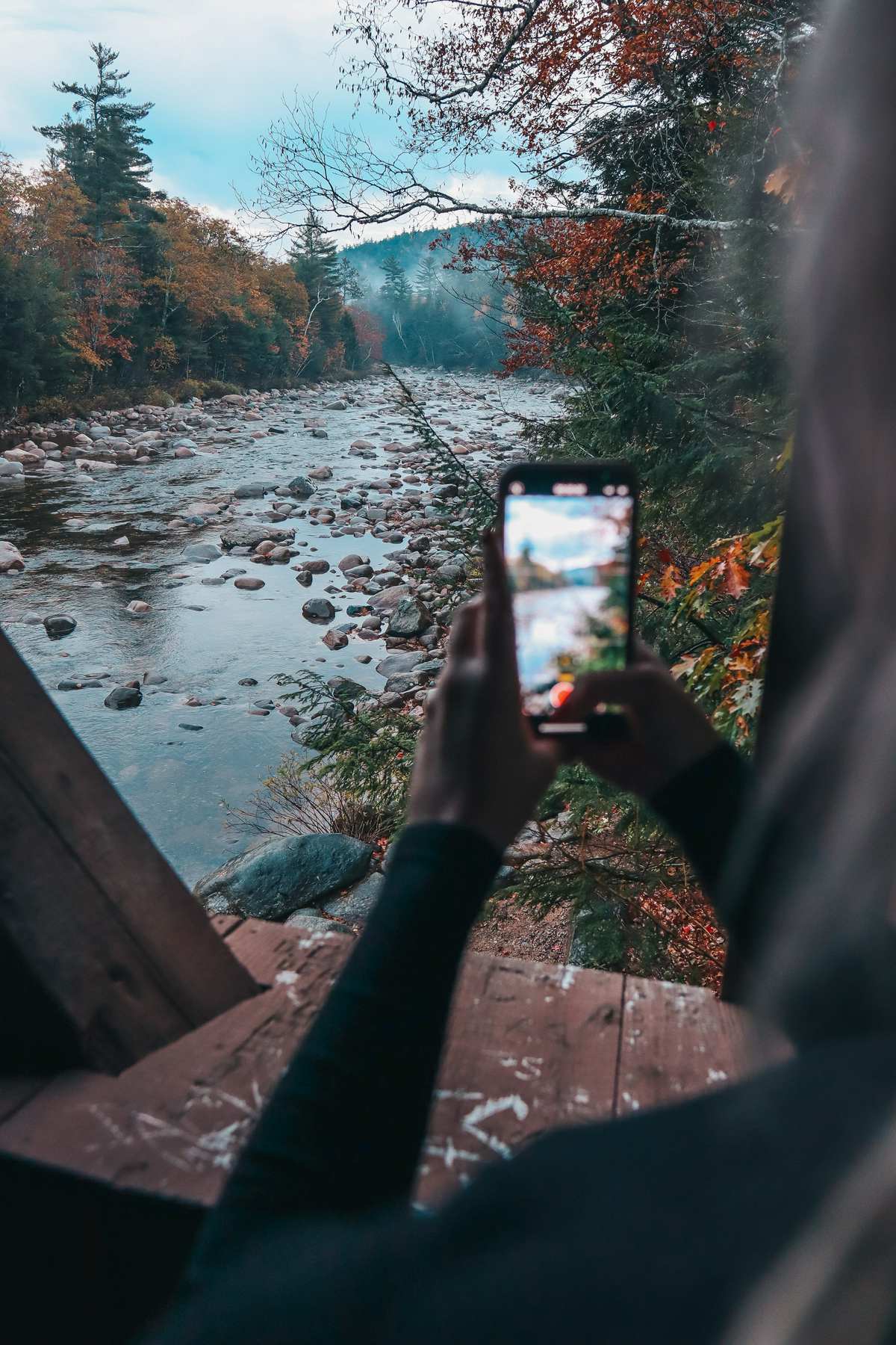 Someone taking a photo with their iPhone at the Albany Covered Bridge in the fall