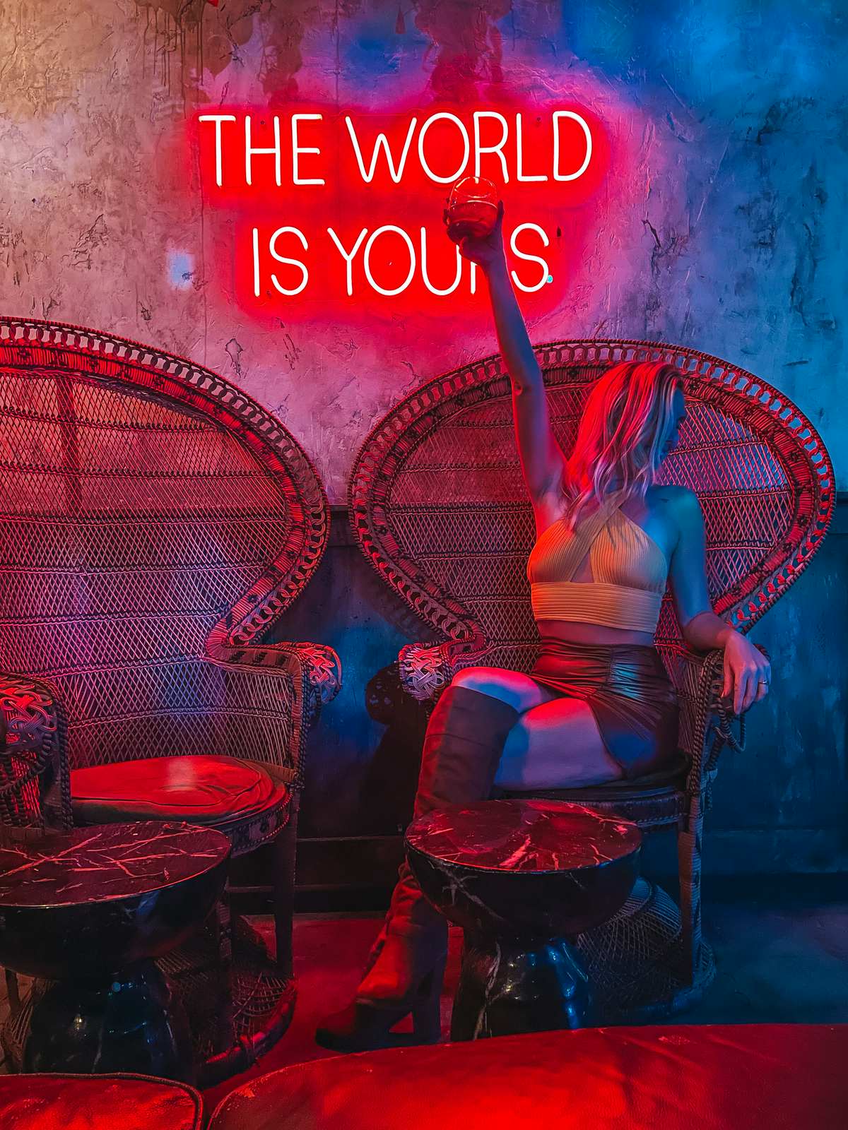 Woman holding up a cocktail at Dirty Laundry bar in St Pete with "The World is Yours" neon sign behind her