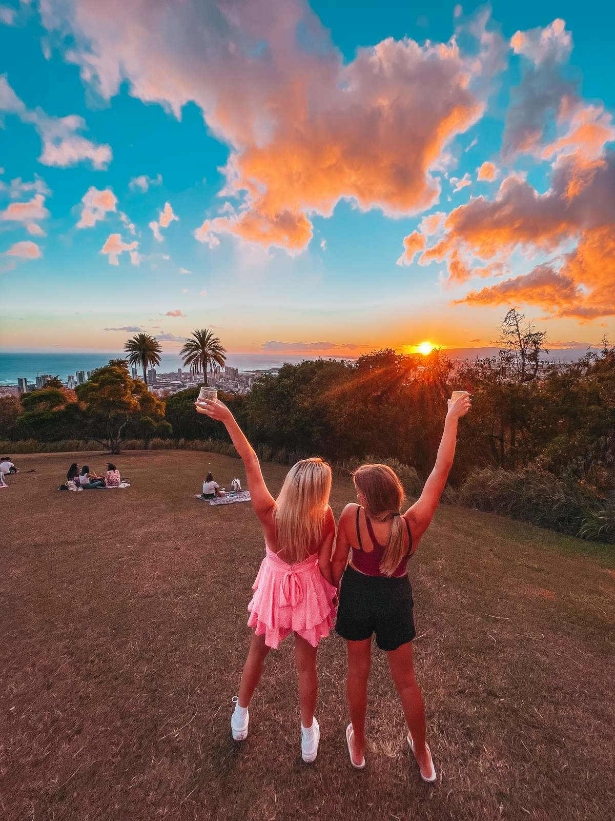 Friends holding up drinks at sunset at Tantalus Lookout on Oahu