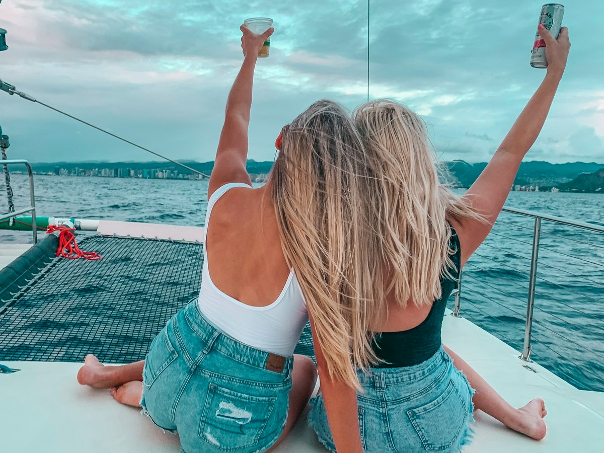 Best friends posing on a boat with drinks in the air on a booze cruise in Waikiki
