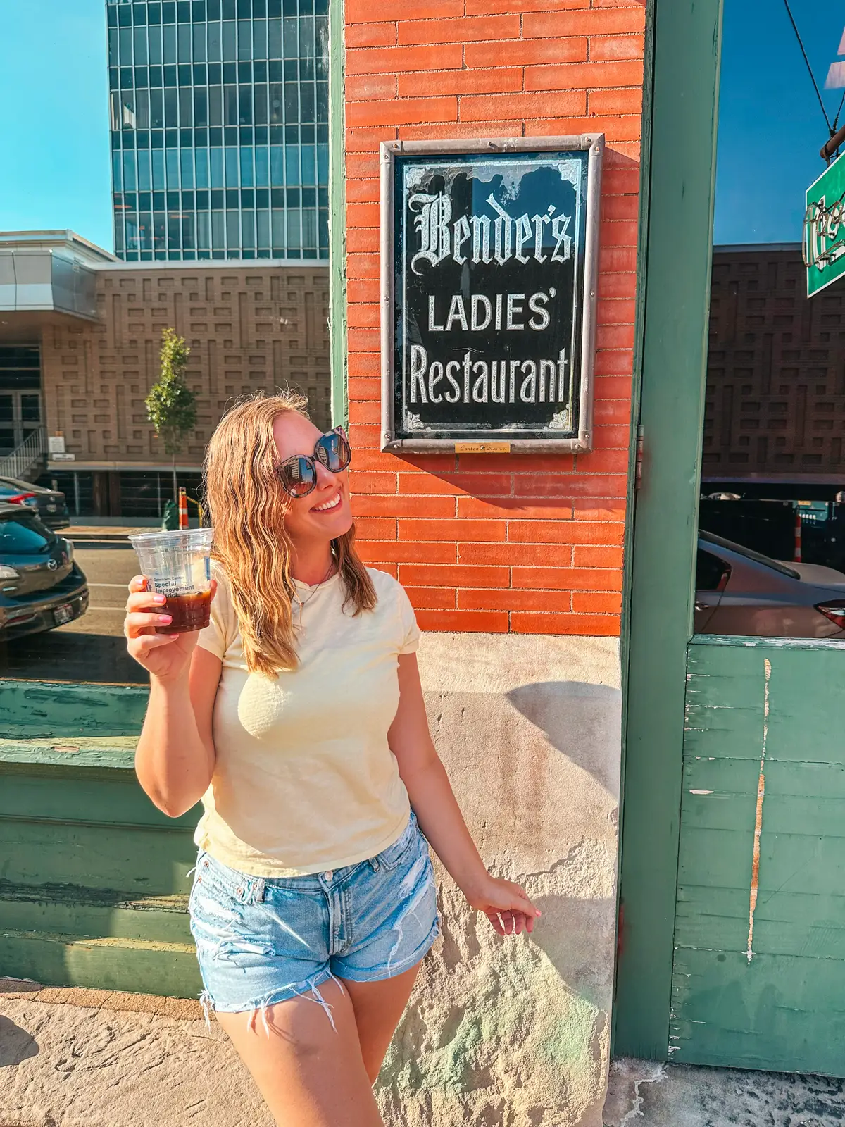 Woman holding to go espresso martini in front of Benders ladies entrance in downtown Canton