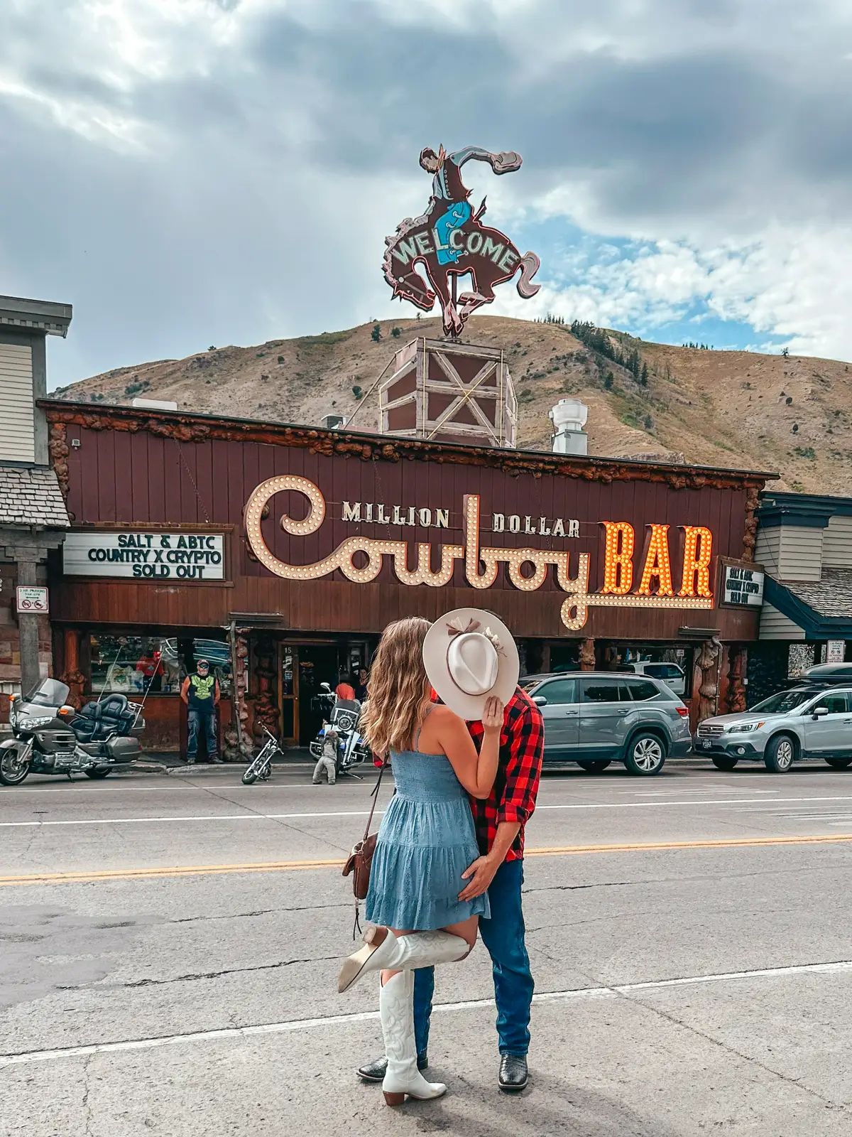 Couple Kissing And Hiding Behind Cowboy Hat In Front Of Million Dollar Cowboy Bar In Jackson Wyoming