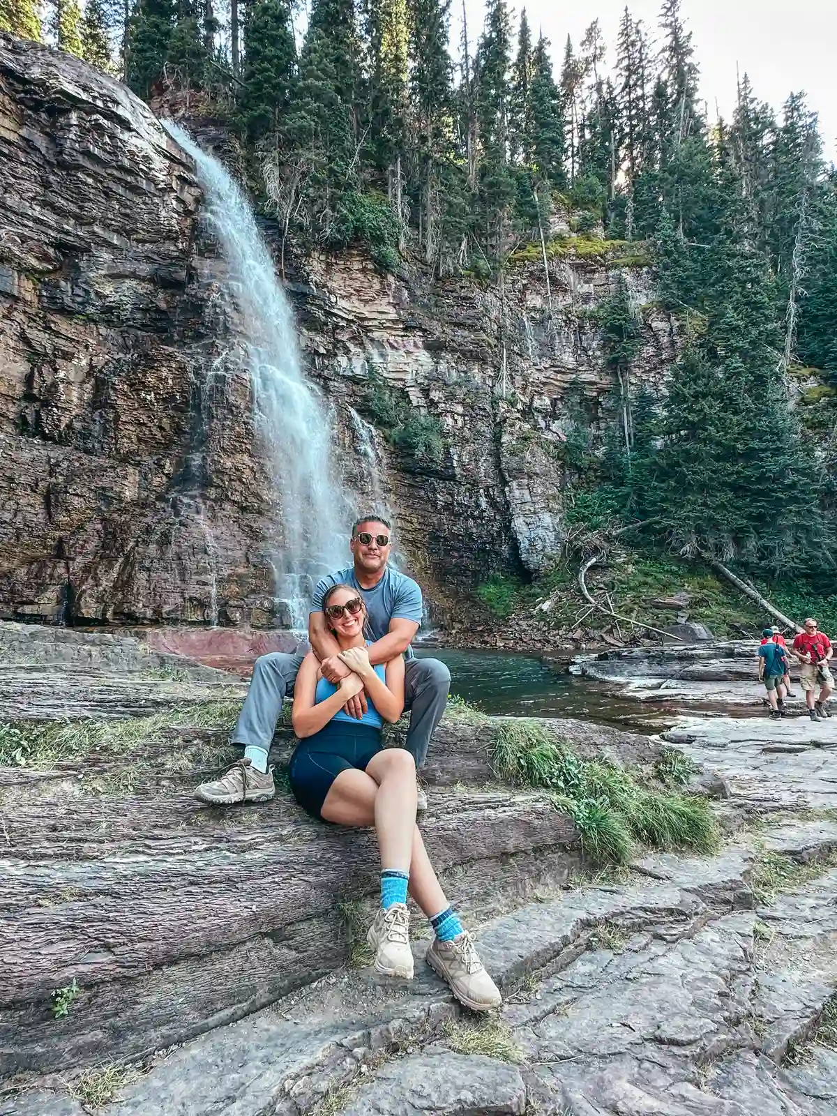 Couple In Front Of Virginia Falls At Glacier National Park In Montana