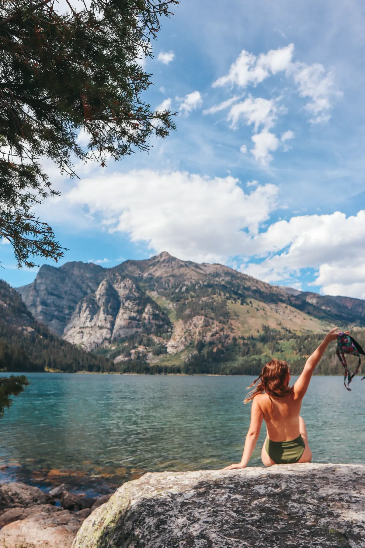Woman Sitting On A Rock Holding Up Bathing Suit Top At Phelps Lake In Grand Teton National Park