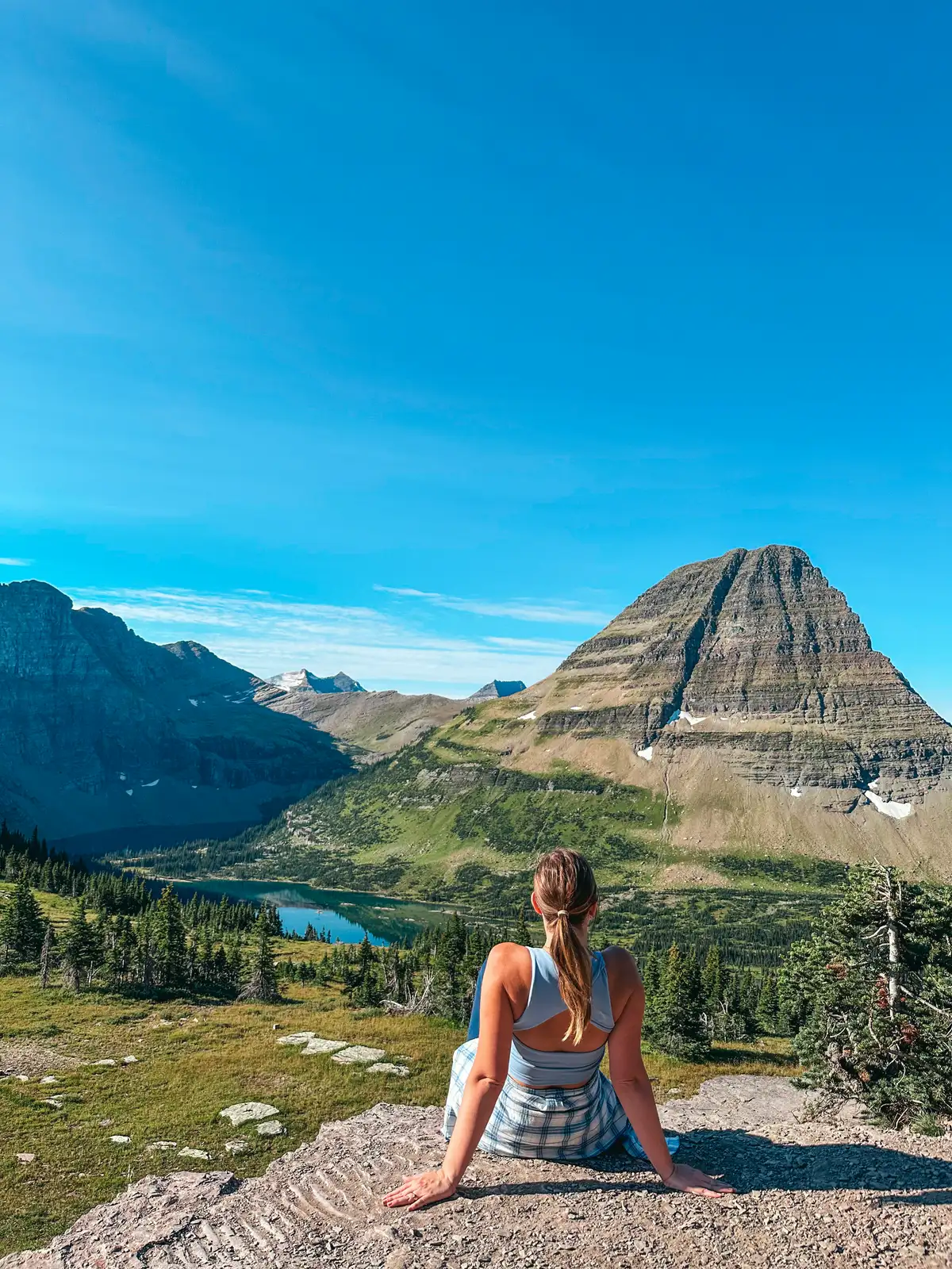 Woman Sitting On A Rock Looking Out At Hidden Lake In Glacier National Park