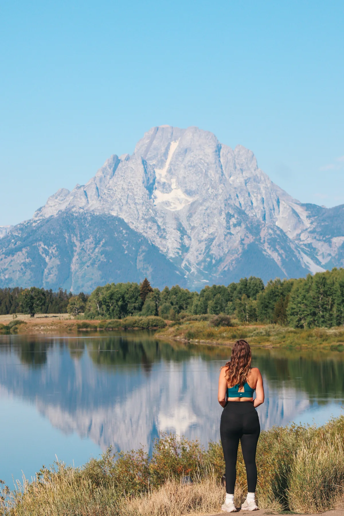 Woman Standing At Oxbow Bend Looking Out At Mount Moran In Grand Teton National Park